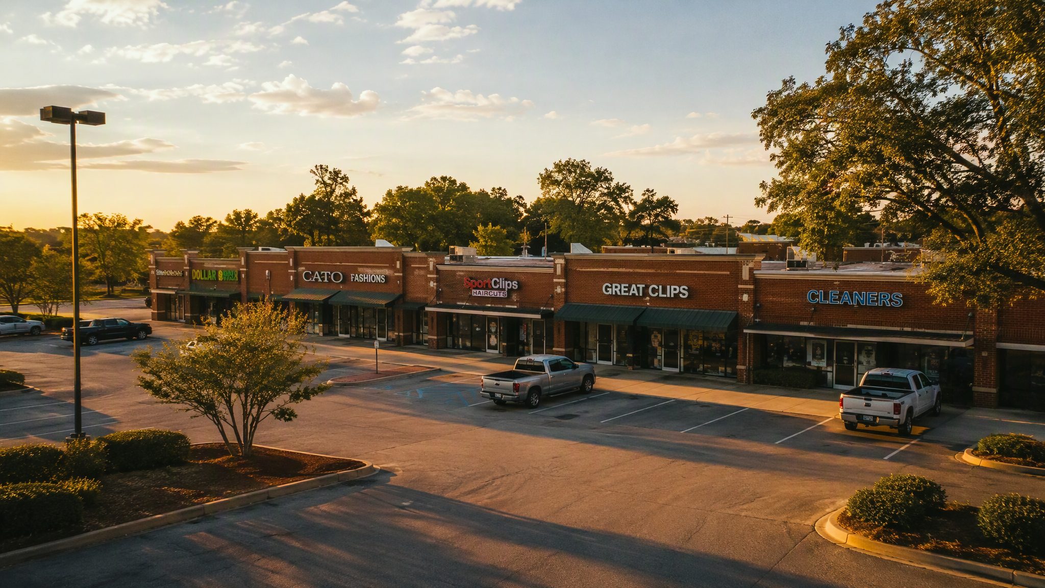 A legacy neighborhood shopping center at golden hour — brick storefronts and a sunlit parking field